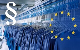Hänge-Förderanlage in einer Wäscherei mit dunkelblauen Kleidungsstücken an Bügeln, darüber ein weißes Paragraphenzeichen und die Sterne der EU-Flagge.